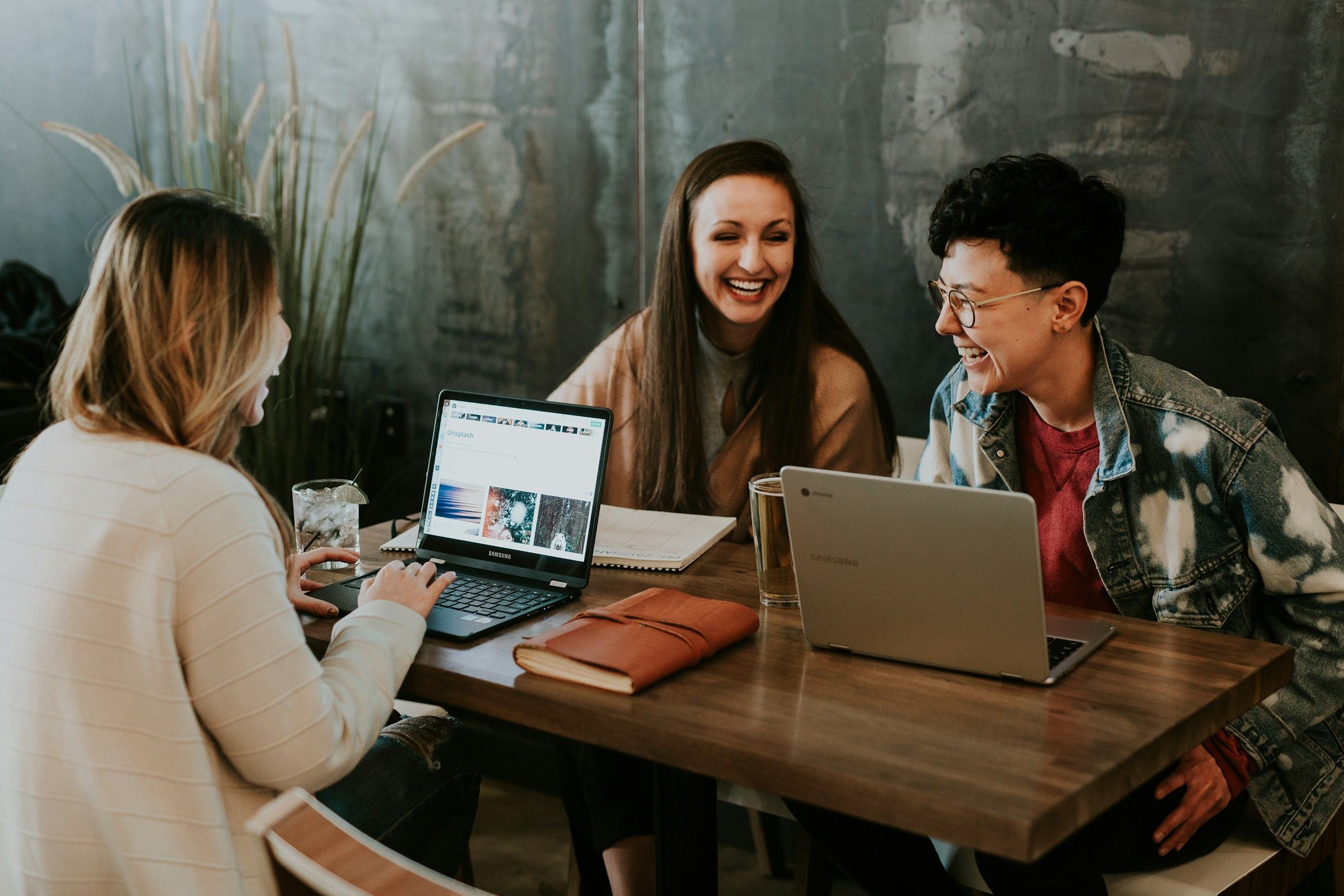 Three people laughing together around laptops at a café table.